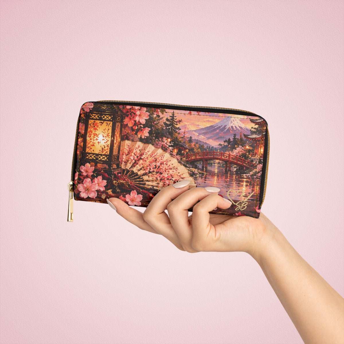 Madama Butterfly — A Thousand Petals zipper wallet held in one hand against a pink background, showing cherry blossoms, a folding fan, red bridge and mountain.