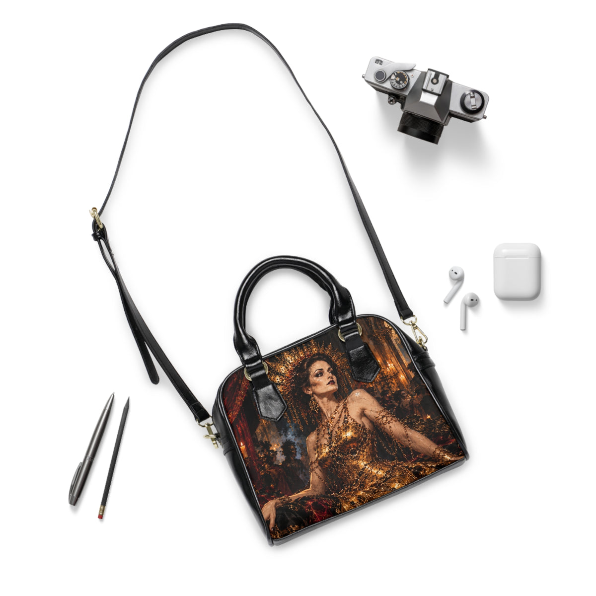 The Gilded Queen shoulder handbag laid flat with its long black strap beside a camera and earbuds.