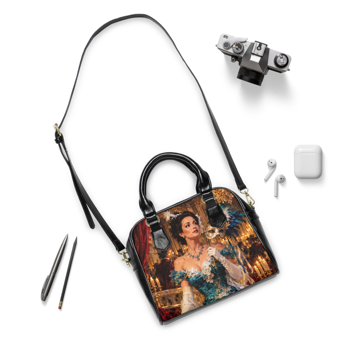 The Masquerade — A Venetian Dream shoulder handbag laid flat with its long black strap beside a camera and earbuds.