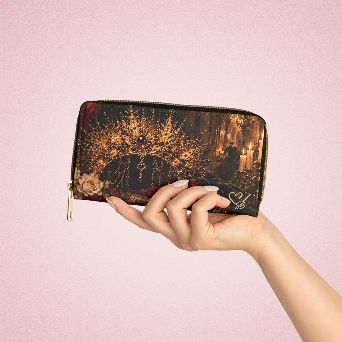 The Gilded Queen zipper wallet held in one hand against a pink background, showing an ornate gold crown, cream rose and candlelight.