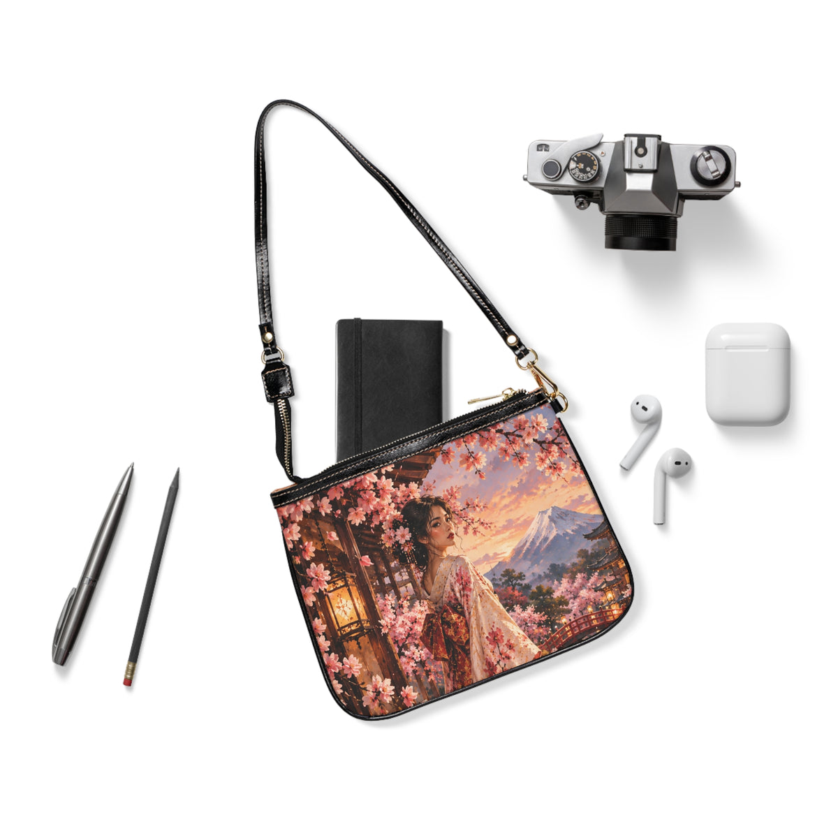 Madama Butterfly — A Thousand Petals small shoulder bag laid flat with its black strap beside a camera, notebook and earbuds.